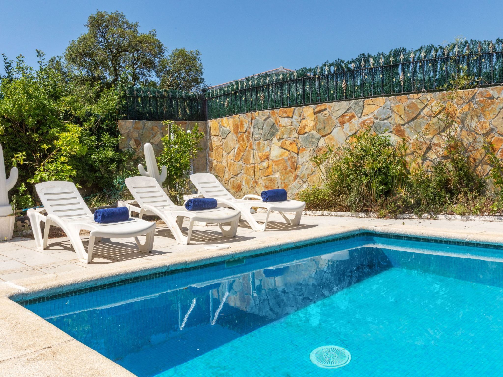 Une piscine bordée de chaises longues blanches et d’un mur en pierre.