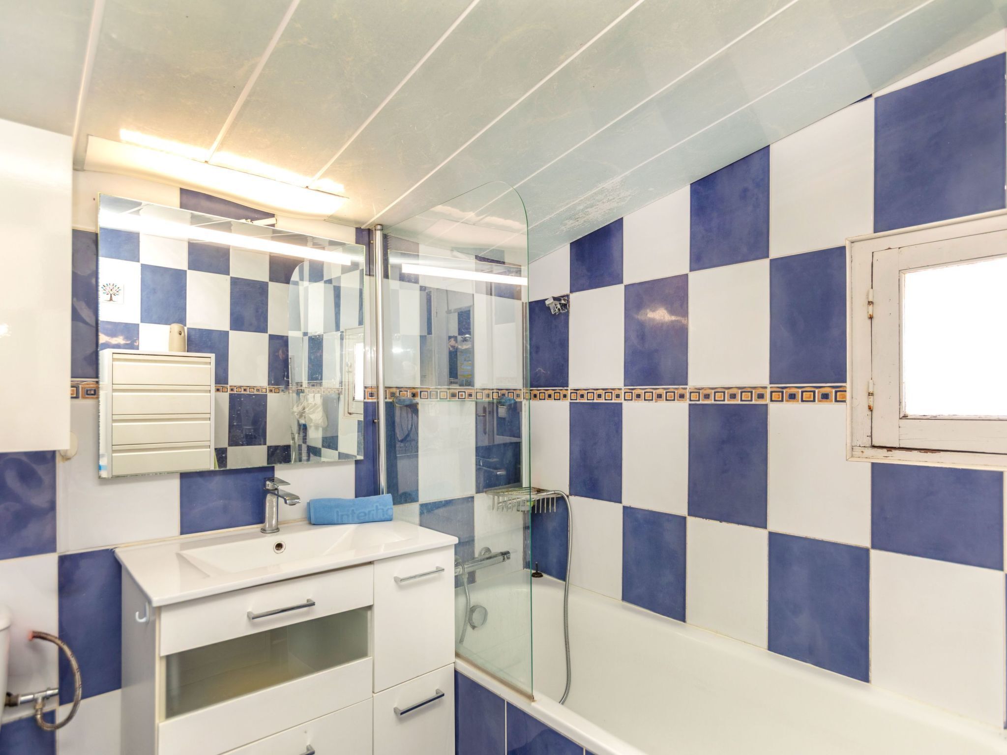 Un baño con pared de baldosas a cuadros, un espejo, un lavamanos y una ducha.