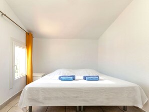 A single bed with a white mattress and two blue pillows, a window with a curtain, and a door. - Vacation home Tuli by Interhome (Lloret de Mar)