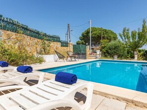 Piscina com espreguiçadeiras e toalhas, cercada por muros de pedra e vegetação.