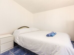 A single bed with white bedding and two rolled towels, a white bedside table, and a blue tiled floor. - Vacation home Tuli by Interhome (Lloret de Mar)
