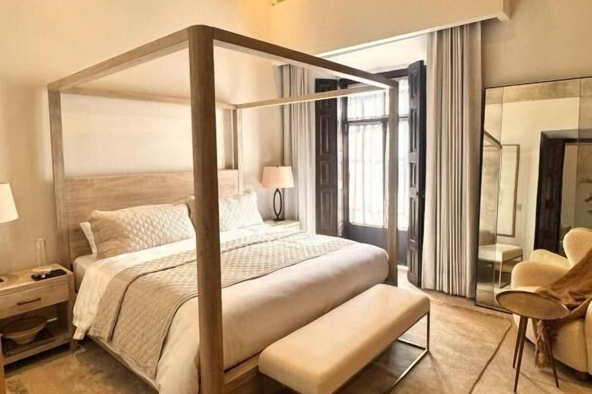 Una cama con dosel, un banco, mesitas de noche, una lámpara y una silla en una habitación de hotel moderna.