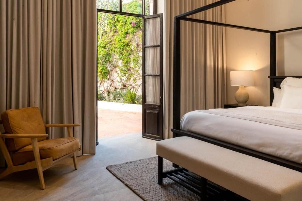 Een slaapkamer met een hemelbed, een stoel en uitzicht op groen buiten.