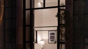 Un portail en arc donne accès à une chambre à coucher qui contient un lit, une table de chevet et une lampe fixée au mur.