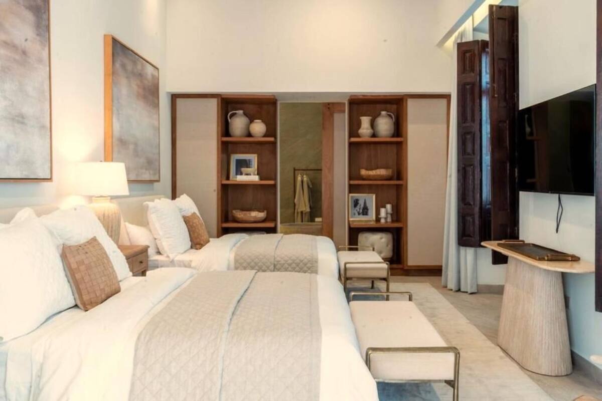 Habitación de hotel con dos camas, televisión, escritorio y estantes con objetos decorativos.