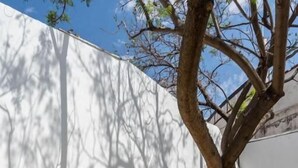Une piscine avec des marches menant à une porte, entourée d’un bâtiment blanc, et un arbre qui projette des ombres.