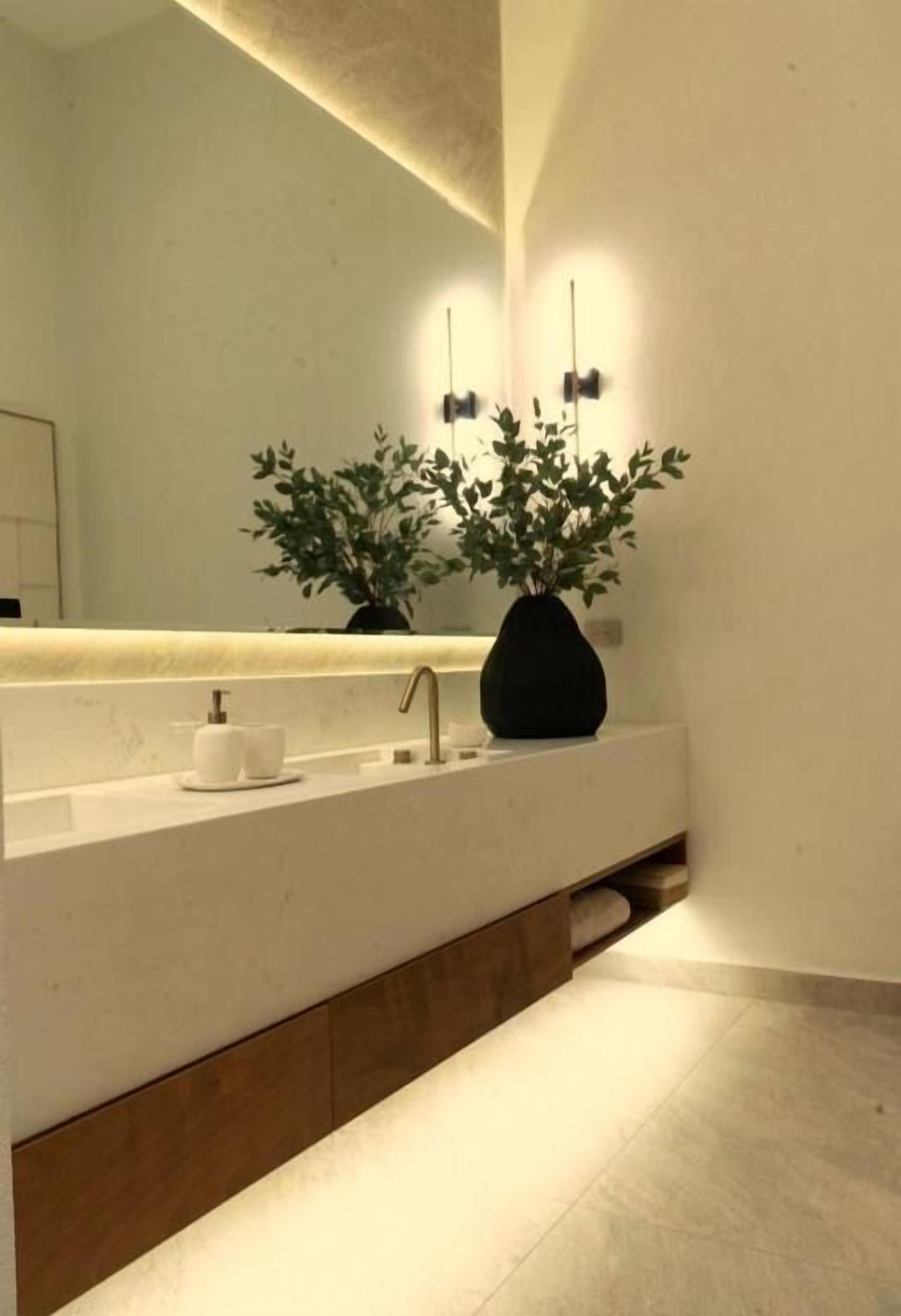 Un baño moderno con una encimera blanca, un florero negro con plantas, un espejo y un perchero para toallas.