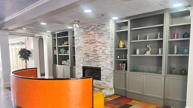 Eine moderne Lobby mit einer gebogenen, orangefarbenen Rezeptionstheke, einer Wand mit Steinakzenten und einem Kamin.
