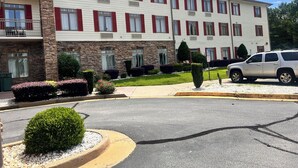 Ein mehrstöckiges Hotel mit Steinverkleidung, roten Fensterläden und einem Parkplatz mit einem weißen SUV.