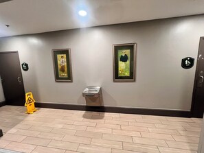 A hallway with two framed pictures on the wall, a trash bin, and a handicap accessibility sign.