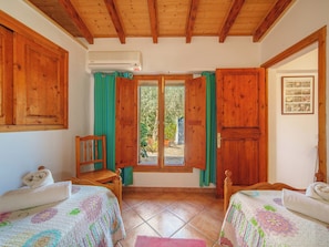 Ein Zimmer mit zwei Betten, Holzbalkendecke, Klimaanlage, einem Fenster mit Vorhängen und einer Tür.