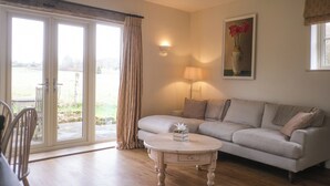 Ein Wohnzimmer mit einer Couch, einem runden Couchtisch, einer Lampe, einem Gemälde und einer Glastür zum Außenbereich.