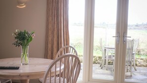 Ein Essbereich mit Tisch, Stühlen, einer Blumenvase und Blick durch eine Glastür ins Freie.