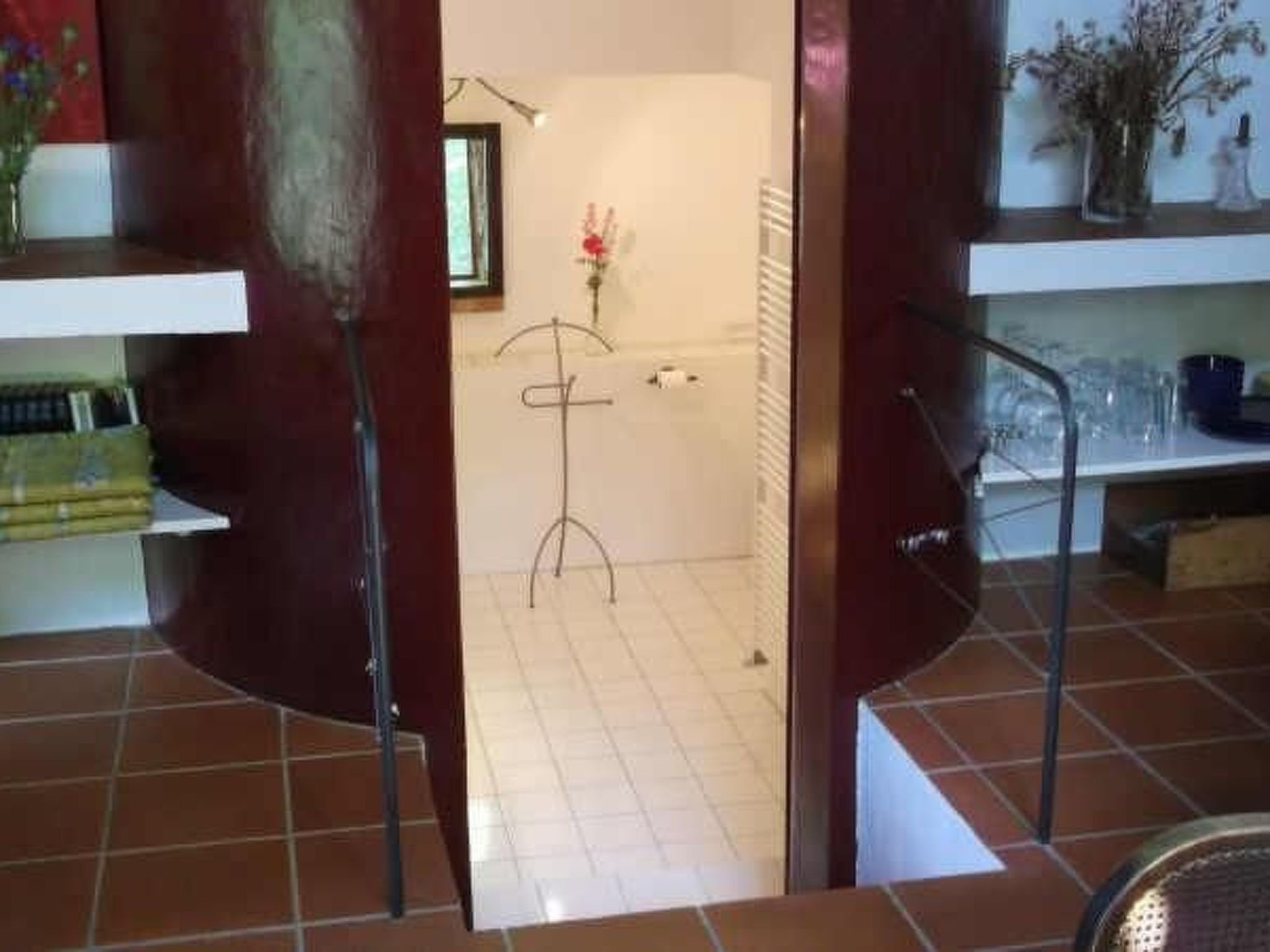 A room with a tiled floor, a wooden door, and a shelf with various items.
