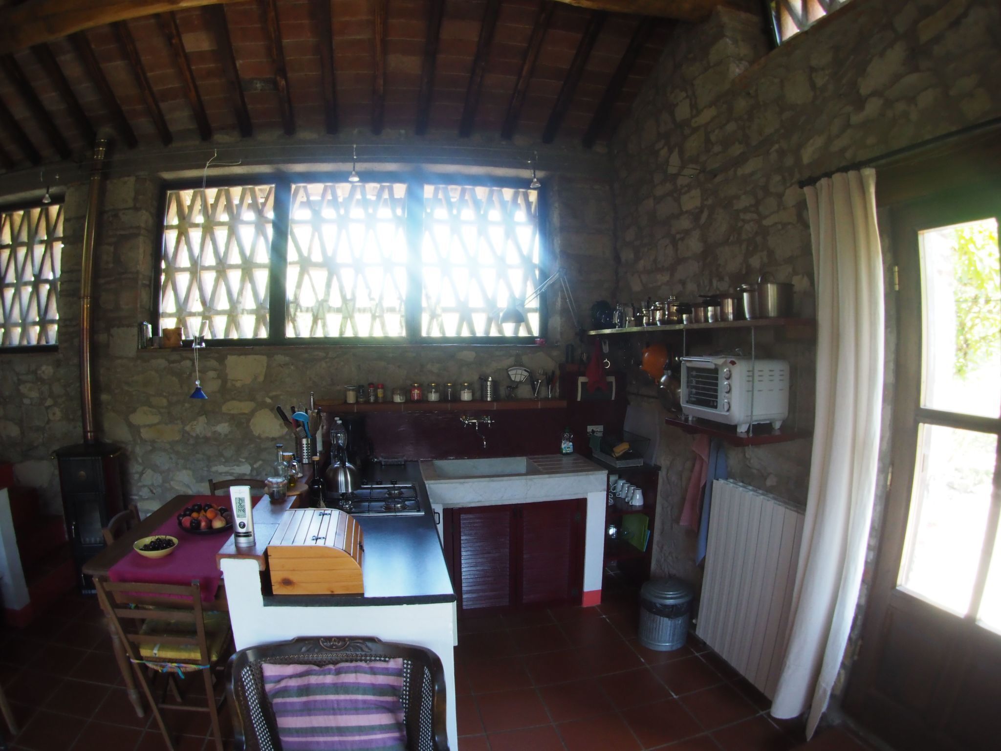 A rustic kitchen with a stone wall, wooden beams, a window with a lattice, a sink, a stove, and a vintage radio.