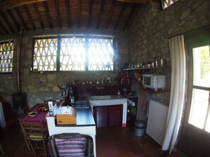 Eine rustikale Küche mit einer Steinwand, Holzbalken, einem Fenster mit Gitterwerk, einer Spüle, einem Herd und einem Vintage-Radio.