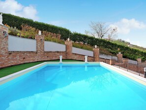 A swimming pool with a brick wall, a white statue, and a hedge. - Sweet Life by Interhome (Priocca)