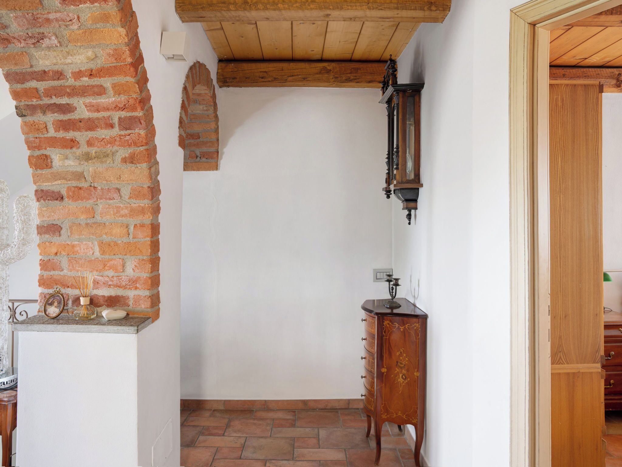 Ein schmaler Korridor mit Backsteinwand, Holzboden und einem an der Wand befestigten Uhrenschrank.
