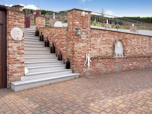 A brick building with a staircase leading to a door, a sign reading 'LA DOLCE,' and a small shelf with decorative items. - Sweet Life by Interhome (Priocca)