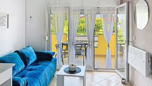 A room with a blue sofa, a small table with a hat, a radiator, and a view through a glass door to an outdoor area with a table and chairs. - Rondine by Interhome (Novigrad (Istra))