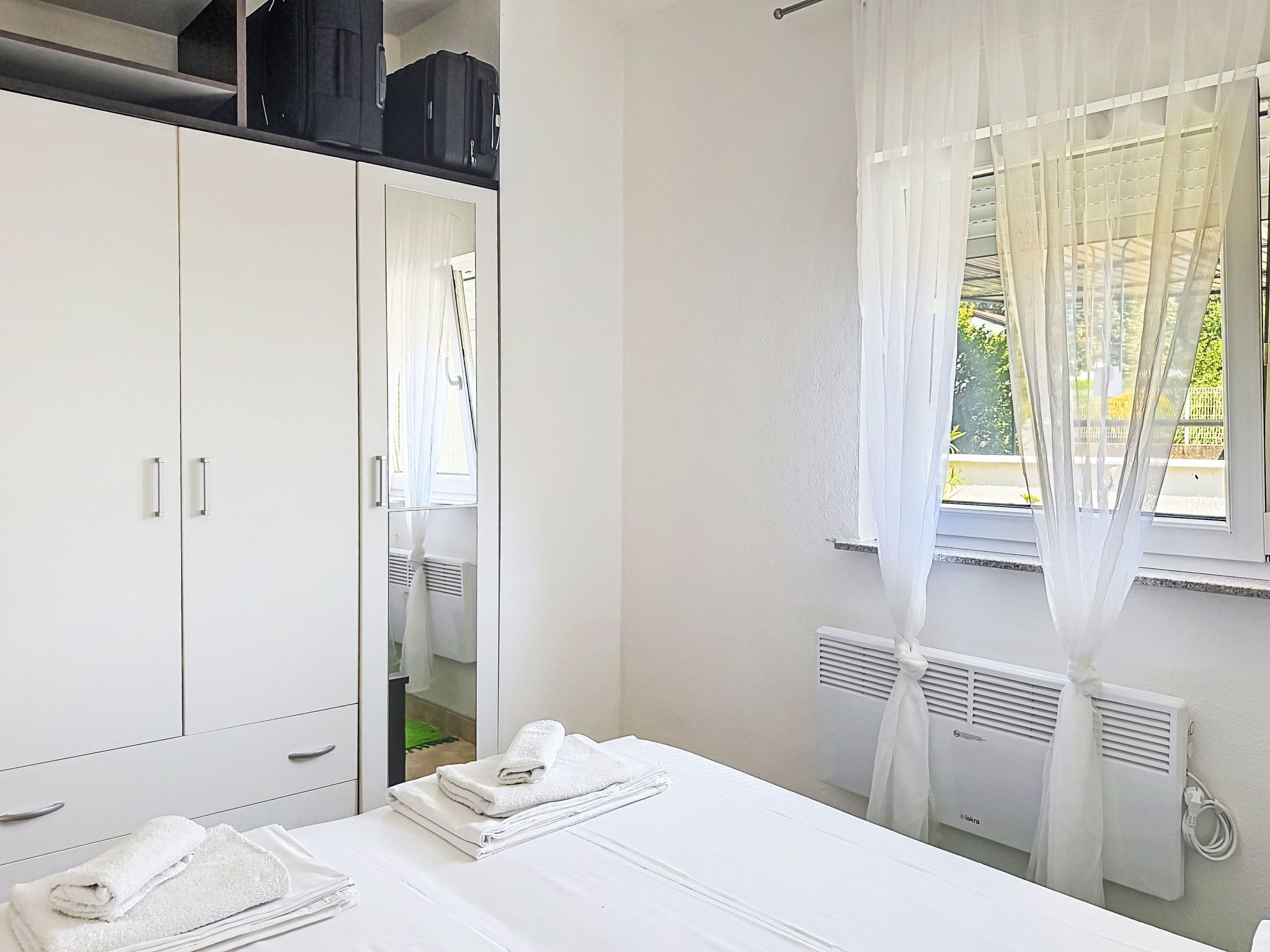 Une chambre d’hôtel avec un lit, une armoire, un radiateur et une fenêtre avec des rideaux légers.