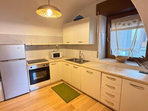 A compact kitchen with a microwave, oven, sink, and a hanging light fixture. - Casa Le Pale by Interhome (Fiera di Primiero)
