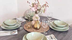 Ett runt matbord med gröna tallrikar och genomskinliga glas, en vas med blommor och en vävd bordsduk.
