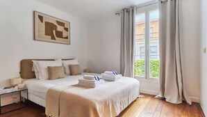 Quarto de hotel com uma cama, mesa de cabeceira, janela com cortinas e um quadro na parede.