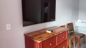 A room with a flat-screen TV mounted on the wall, a wooden dresser with drawers, a chair, and a small table with a remote control. - Mountain Inn (Gatlinburg)