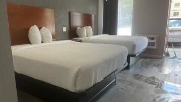 A hotel room with two beds, a wooden headboard, a window with curtains, and an air conditioning unit.