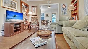 A living room with a television, bookshelves, a sofa, a dining table, and a chair.