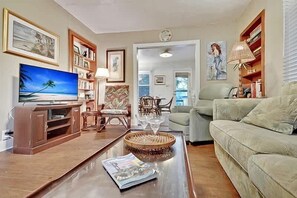 Ein Wohnzimmer mit Fernseher, Bücherregalen, einer Couch, einem Esstisch und einem Stuhl.