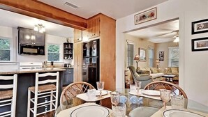 A modern kitchen with wooden cabinets, a dining area with a table set for four, and a view into the living room.