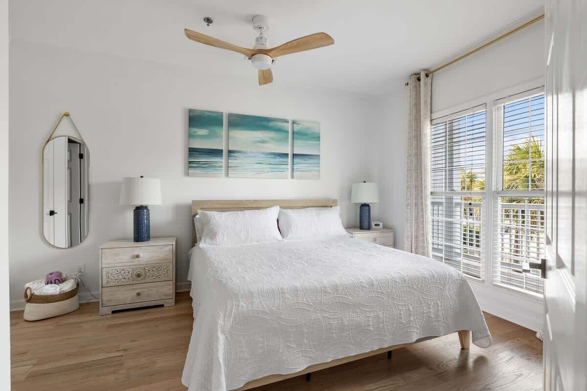 Een slaapkamer met een bed, twee nachtkastjes, een plafondventilator, een raam met jaloezieën en een spiegel aan de muur.