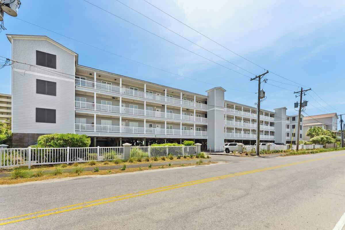 A multi-story hotel with balconies, a parking area, and a clear sky.