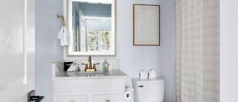 Un baño con tocador blanco, inodoro, una obra de arte enmarco y ventana con vistas.