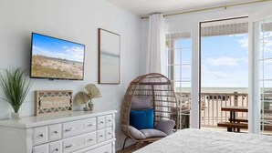 Ein Schlafzimmer mit einem Bett, einem Schminktisch, einem Korbstuhl, einem Fernseher und einem Balkon mit Blick.