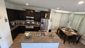 A kitchen with dark cabinets, a granite countertop island, stainless steel appliances, and a dining area with a table and chairs. - Pleasant 3-bedroom house with AC in charming Odessa, maximum guest 6. (Odessa)