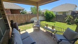 Un patio cubierto con mobiliario exterior, una valla de madera y vistas a un barrio residencial.