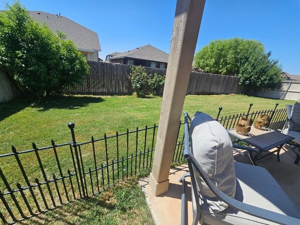 Un patio trasero con una terraza, una cerca de metal y una casa al fondo.