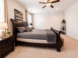 Ein Schlafzimmer mit Bett, Nachttisch, Lampe, Deckenventilator und Wandbildern.