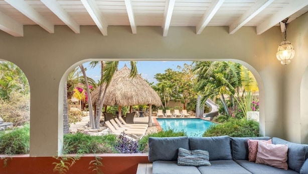 A poolside area with a sofa, a thatched umbrella, and a slide. - Villa Nirvana 6BR Private Family, Pool & Bar Villa (Noord)