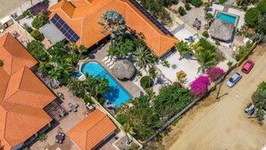 An aerial view of a resort with multiple buildings, a swimming pool, and a beach area. - Villa Nirvana 6BR Private Family, Pool & Bar Villa (Noord)