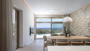 Ein moderner Essbereich mit großem Tisch und Stühlen, einer Steinwand und Blick ins Freie.