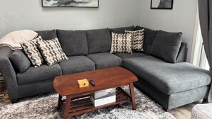 Un sofá seccional gris con almohadones estampados, una mesa de centro de madera y dos obras de arte enmarcadas en la pared.