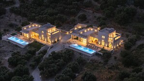 Eine moderne, mehrstöckige Villa mit Swimmingpool, umgeben von Bäumen und Hügeln.