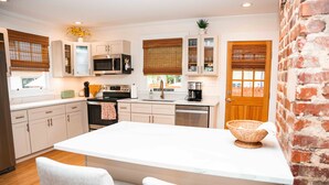 A kitchen with white cabinets, a central island, and a brick wall. - Safe and quiet street. Walk to shops & more. Fenced in yard w huge front porch.  (Charlotte)