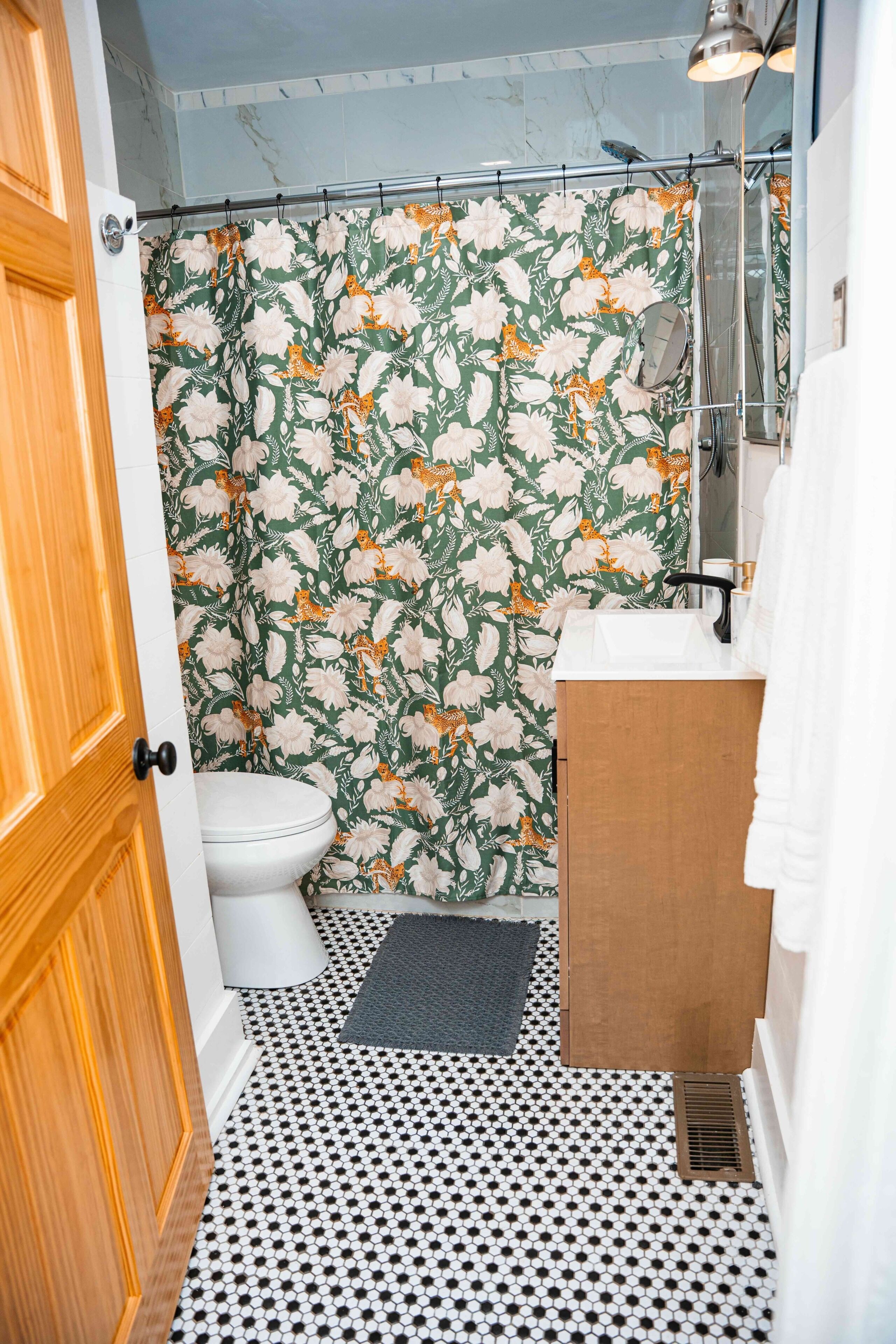 Un baño con inodoro, ducha, lavabo y cortina de ducha estampada.