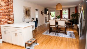A kitchen with wooden flooring, a white island with drawers, a dining area with chairs, and a refrigerator. - Safe and quiet street. Walk to shops & more. Fenced in yard w huge front porch.  (Charlotte)