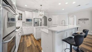 A modern kitchen with white cabinetry, a central island, bar stools, and a welcome sign. - Fantastic 4-bedroom house with AC in tranquil Cordova (Cordova)